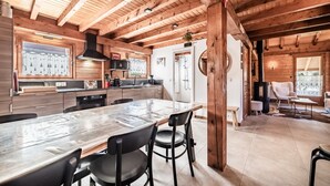 A wooden cabin interior with a large dining table, kitchen area, and a cozy seating area. - Chalet “6p Premium - Zibeline” with Mountain View, Private Terrace, and Wi-Fi (Verchaix)