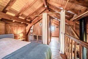 A wooden cabin bedroom with a bed, a nightstand, a lamp, a wooden bench, and a staircase leading to an upper level. - Chalet “6p Premium - Zibeline” with Mountain View, Private Terrace, and Wi-Fi (Verchaix)