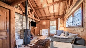 A wooden cabin interior with a fireplace, a sofa, a television, and a stone wall. - Chalet “6p Premium - Zibeline” with Mountain View, Private Terrace, and Wi-Fi (Verchaix)