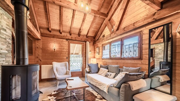 A log cabin interior with a wood-burning stove, a sofa, a chair, and a cowhide rug. - Chalet “6p Premium - Zibeline” with Mountain View, Private Terrace, and Wi-Fi (Verchaix)