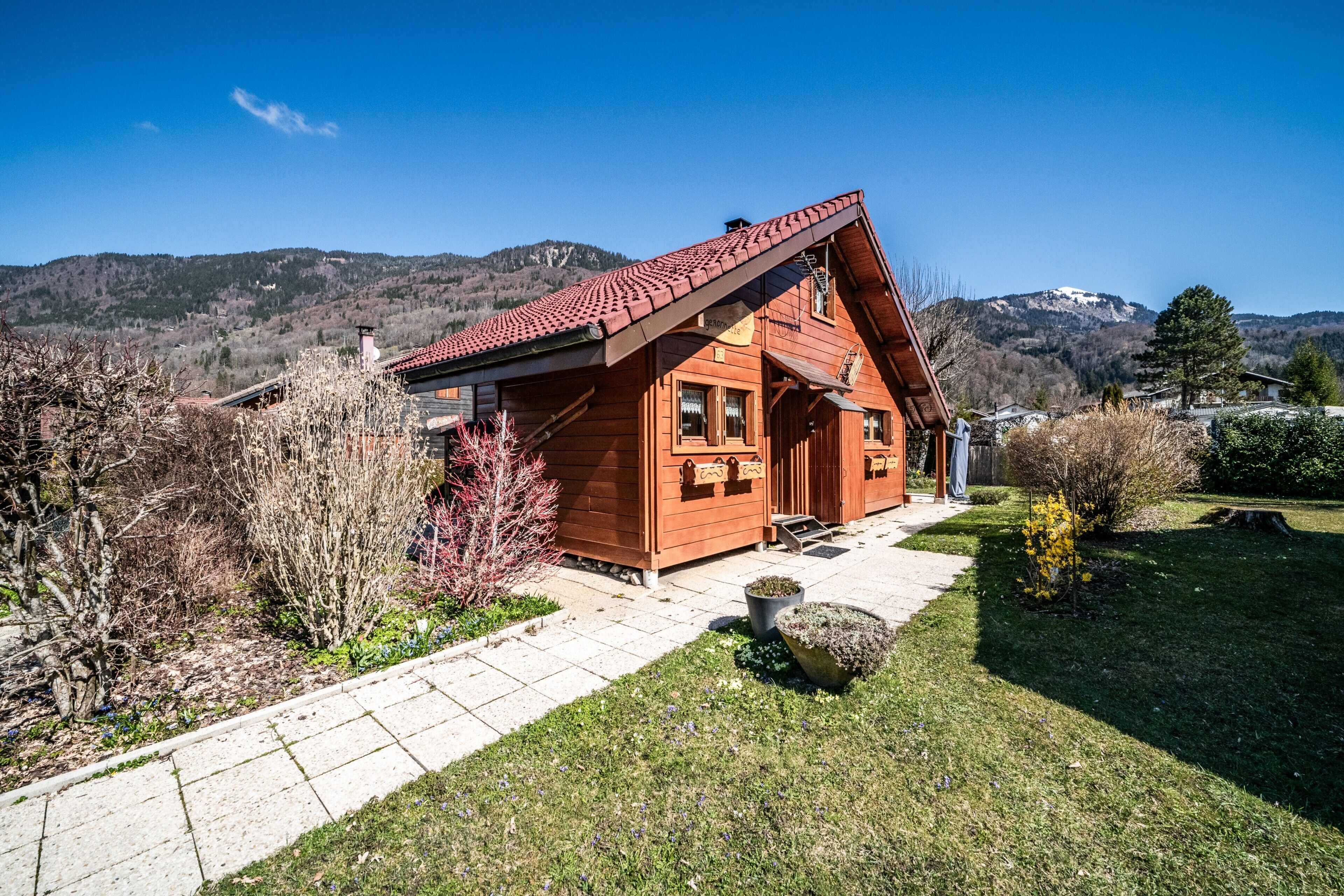 A wooden cabin with a sloped roof, a stone pathway, and a view of mountains.
