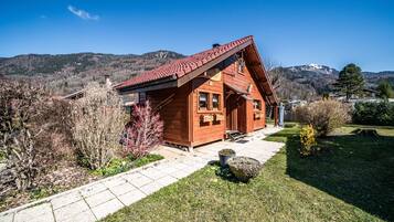 A wooden cabin with a sloped roof, a stone pathway, and a view of mountains.