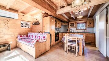 Interno di una baita in legno con divano, tavolo da pranzo, angolo cottura e travi a vista al soffitto.
