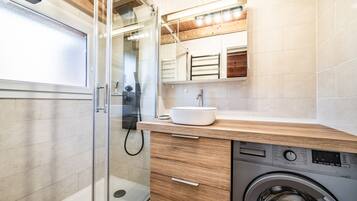 Un baño moderno con cabina de ducha de vidrio, lavadora integrada y tocador de madera con lavamanos.