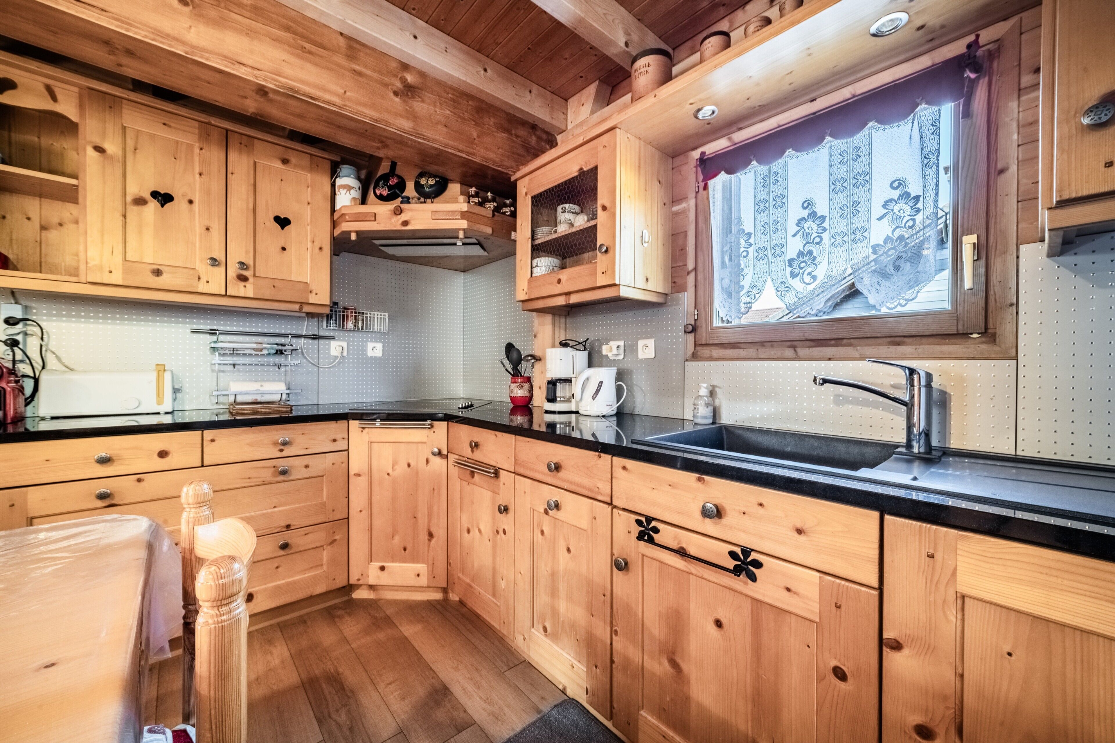 Una cucina in stile baita in legno, con mobili a incasso, un piano di lavoro nero e una finestra con tende in pizzo.