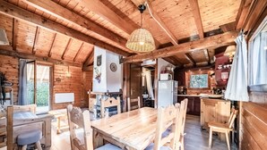 Een houten chalet van binnen, met een eettafel, stoelen, een keukenhoek en een groot raam.