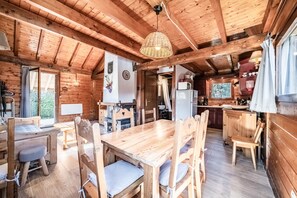 Ein Holzblockhaus im Inneren mit Esstisch, Stühlen, einer Küchenzeile und einem großen Fenster.