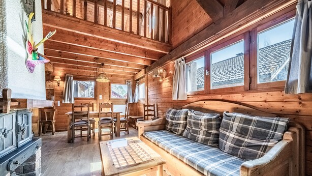 Een houten hut binnen met een bank, eettafel, stoelen en een open haard.