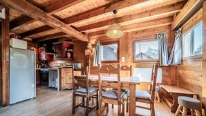 Een houten chalet van binnen, met een eettafel, stoelen, een koelkast en een keukenhoek.