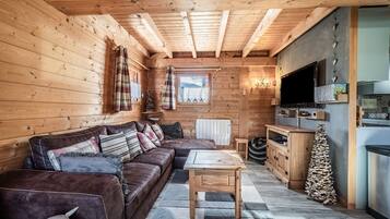 Een houten blokhut van binnen met een bank, tafel, keukenhoek en een raam met uitzicht.