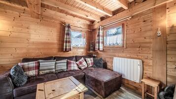 Interior de una cabaña de madera con un sofá, una mesita, un radiador y una ventana.