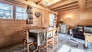 A wooden cabin interior with a dining table, chairs, a sofa, and a chandelier. - Chalet “6p - Le Cocon Des Neiges”: Mountain View, Shared Terrace & Wi-Fi (Verchaix)