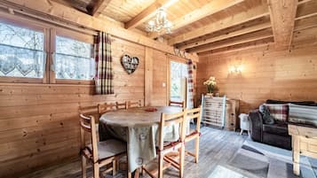 Interior de una cabaña de madera con una mesa de comedor, sillas, un sofá y una araña.