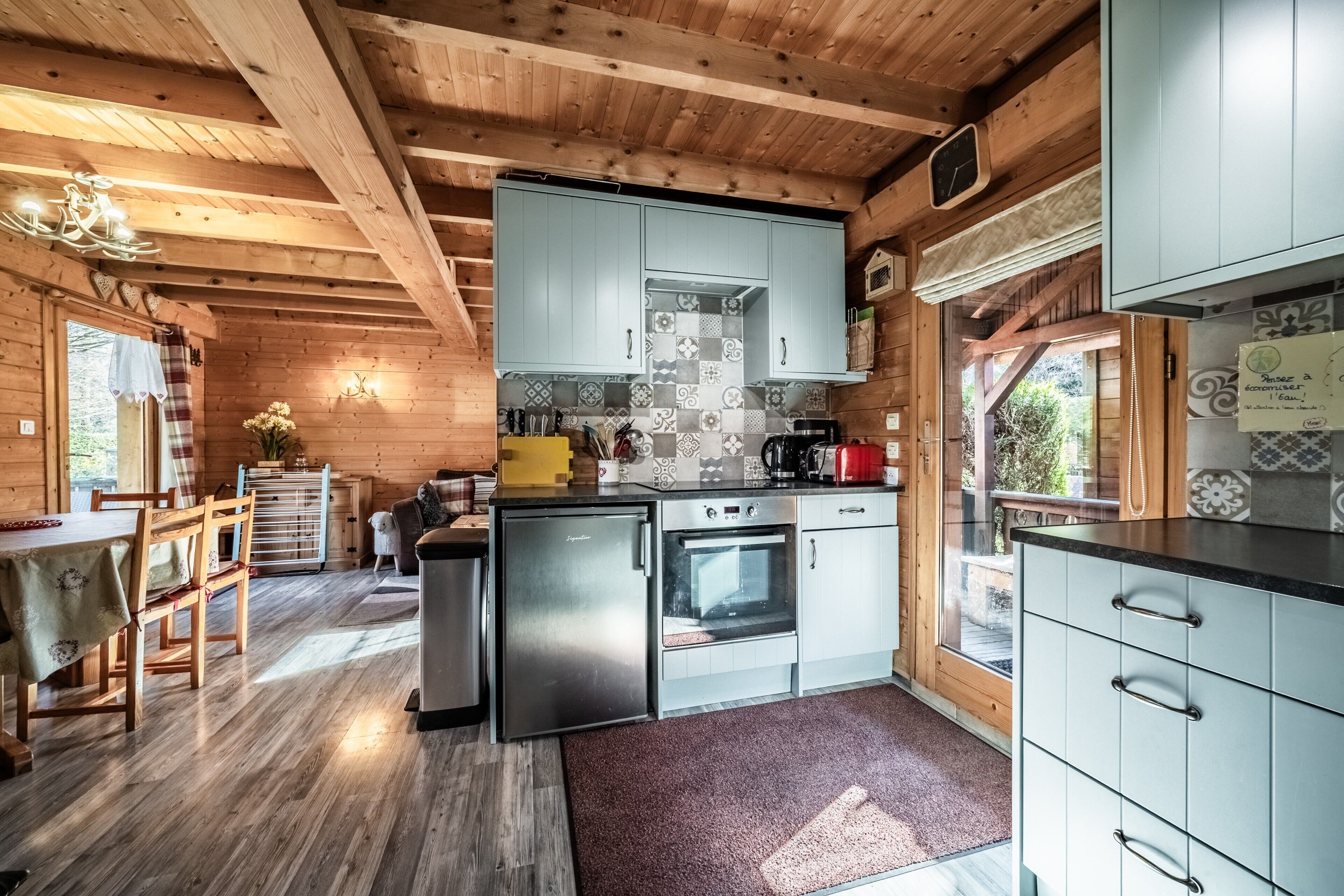 Een houten cabin met keuken, eethoek en uitzicht op de natuur.