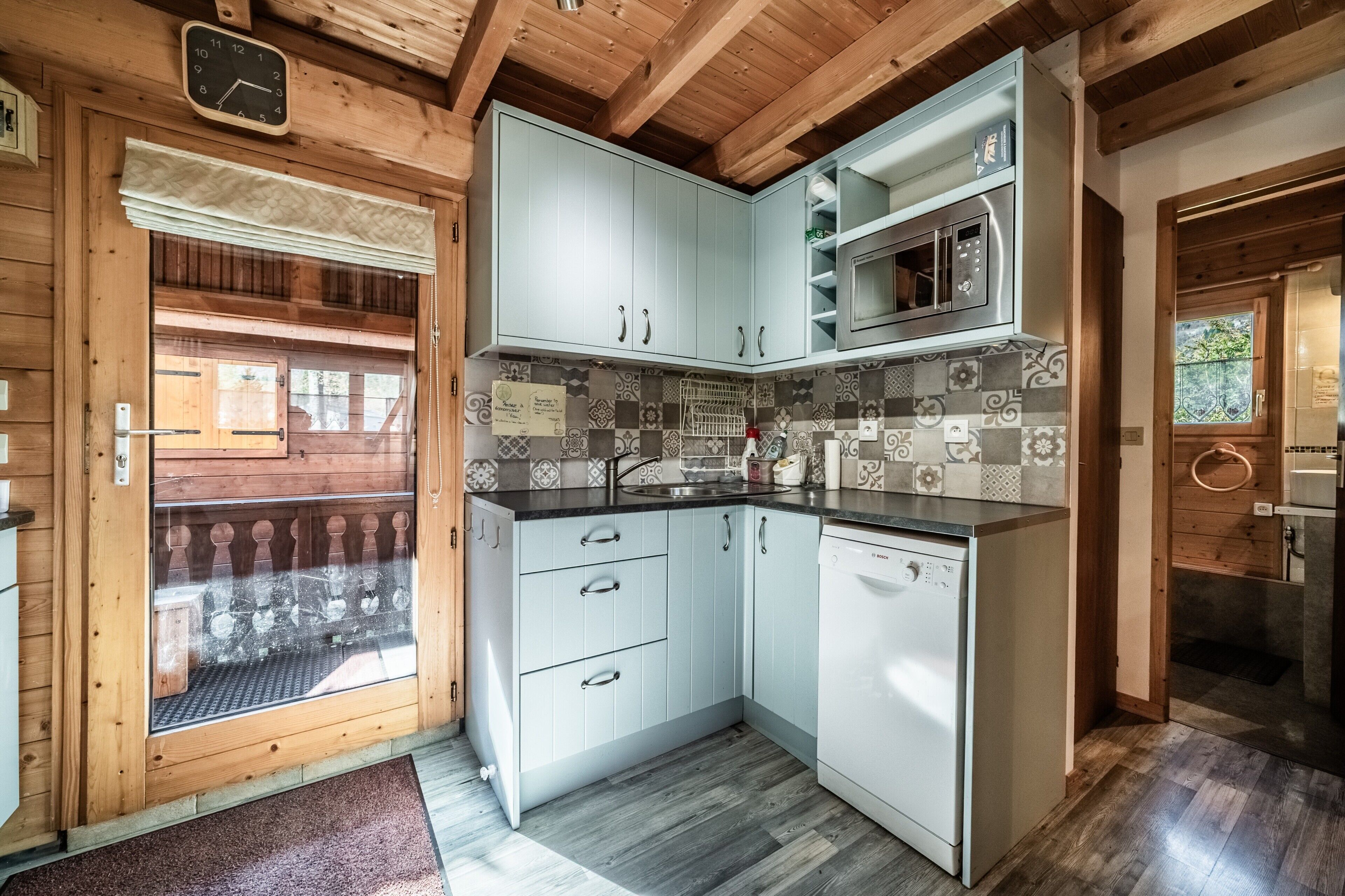 Una cocina con armarios azul claro, un microondas de acero inoxidable y un lavavajillas Bosch.