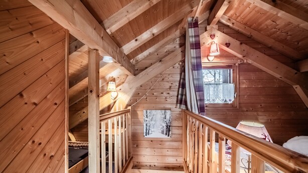 A wooden cabin interior with a loft bedroom, a staircase, and a window with a view. - Chalet “6p - Le Cocon Des Neiges”: Mountain View, Shared Terrace & Wi-Fi (Verchaix)