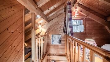 Een houten chalet van binnen, met een slaapkamer op de vide, een trap en een raam met uitzicht.