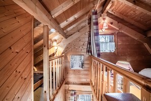 Interior de una cabaña de madera con un altillo, una escalera y una ventana con vistas.