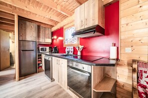 A compact kitchen with wooden cabinets, a stainless steel refrigerator, a microwave, and a dishwasher. - Chalet “6p - Le Refuge Des Lhottis” with Mountain View, Private Terrace & Wi-Fi (Verchaix)