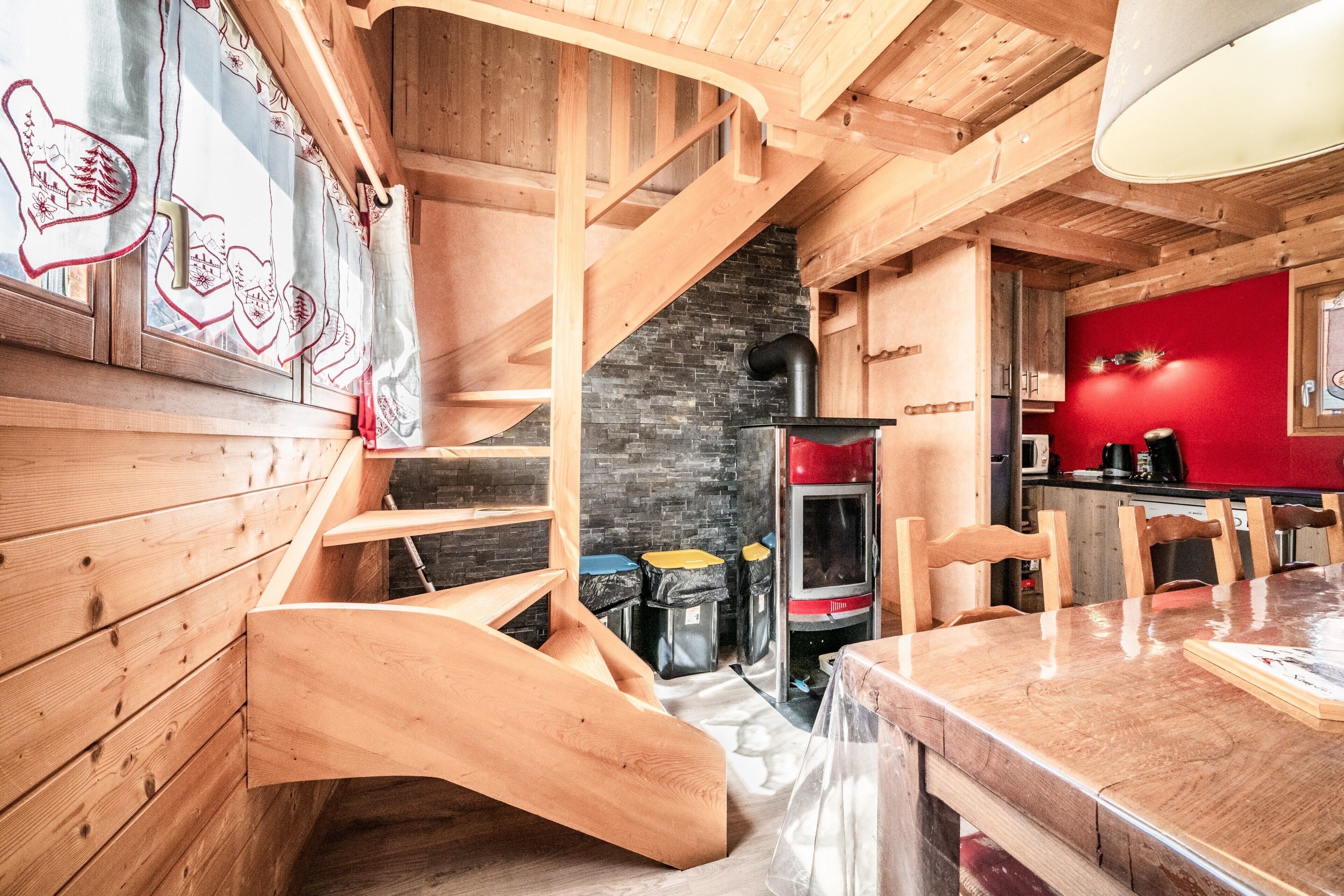 A wooden interior with a staircase, kitchen area, and red wall.