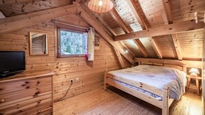 Une chambre à coucher dans un chalet en bois, avec un lit, une commode, une télévision et une fenêtre donnant sur la forêt.