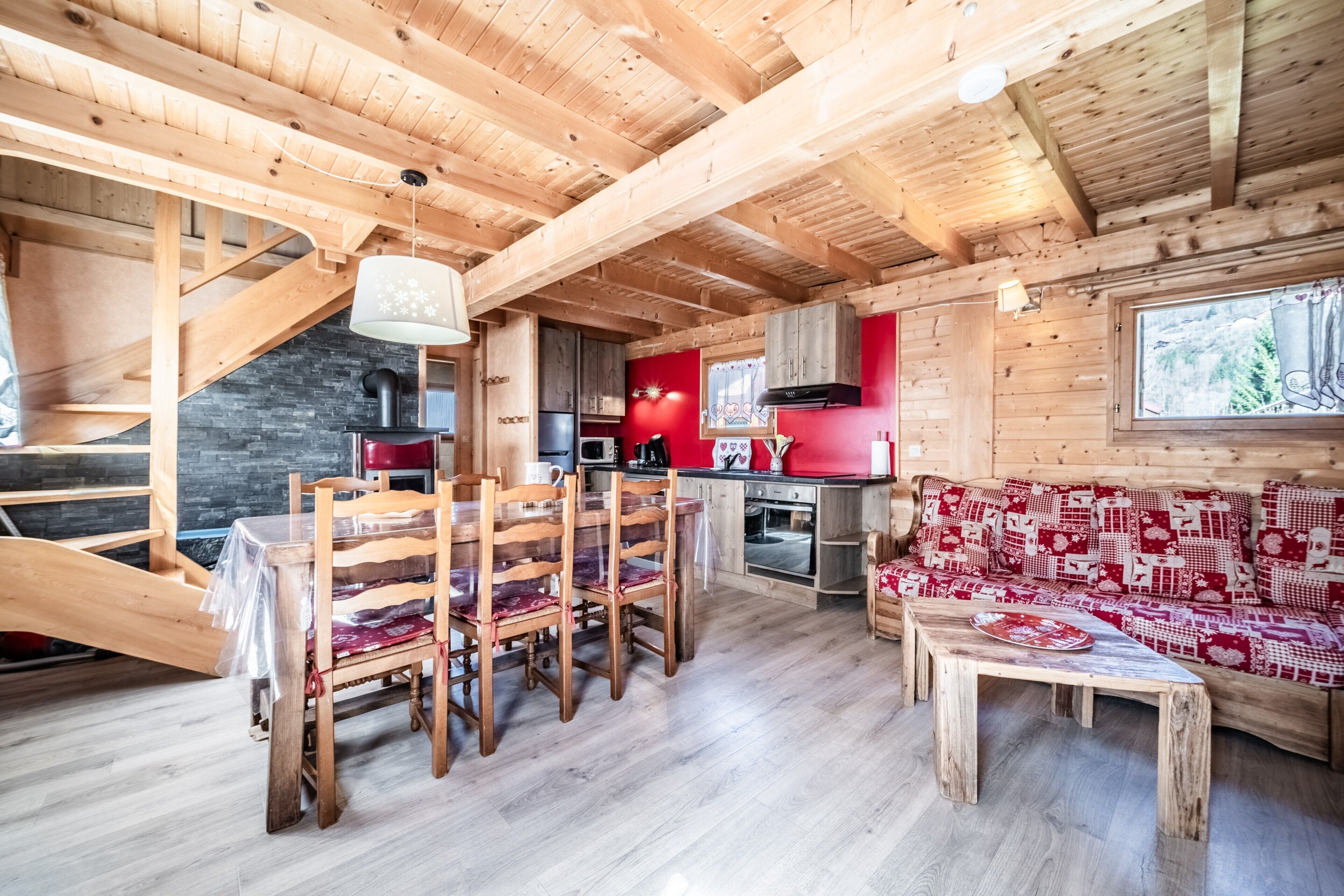 Ambiente in legno con zona pranzo, cucina e un divano rosso con motivo decorativo.
