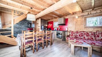 Ambiente in legno con zona pranzo, cucina e un divano rosso con motivo decorativo.