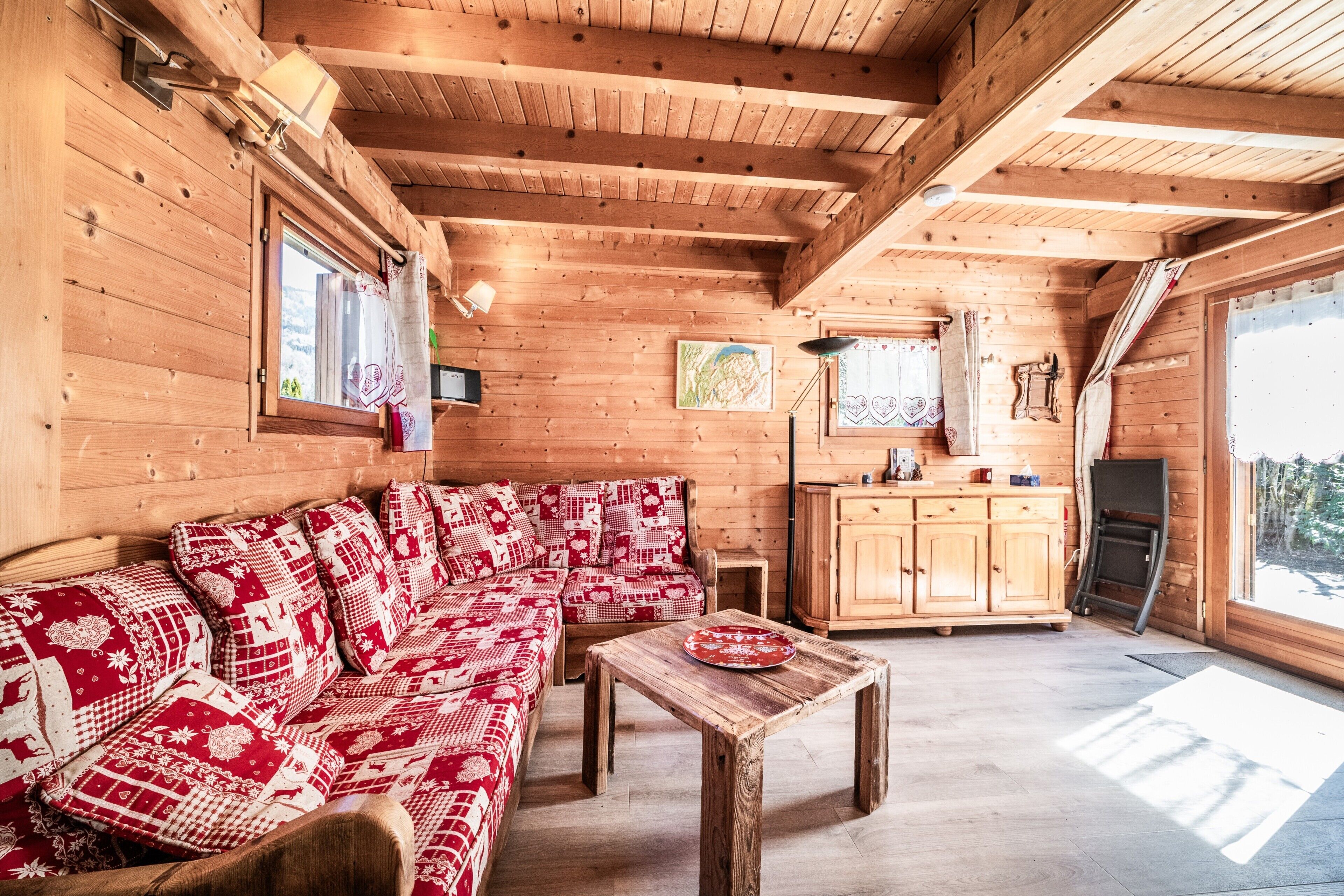 Interior de una cabaña de madera con sofá, mesa y zona de cocina.
