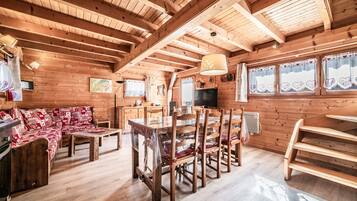 Interno di una baita in legno con tavolo da pranzo, sedie, divano e angolo cottura.