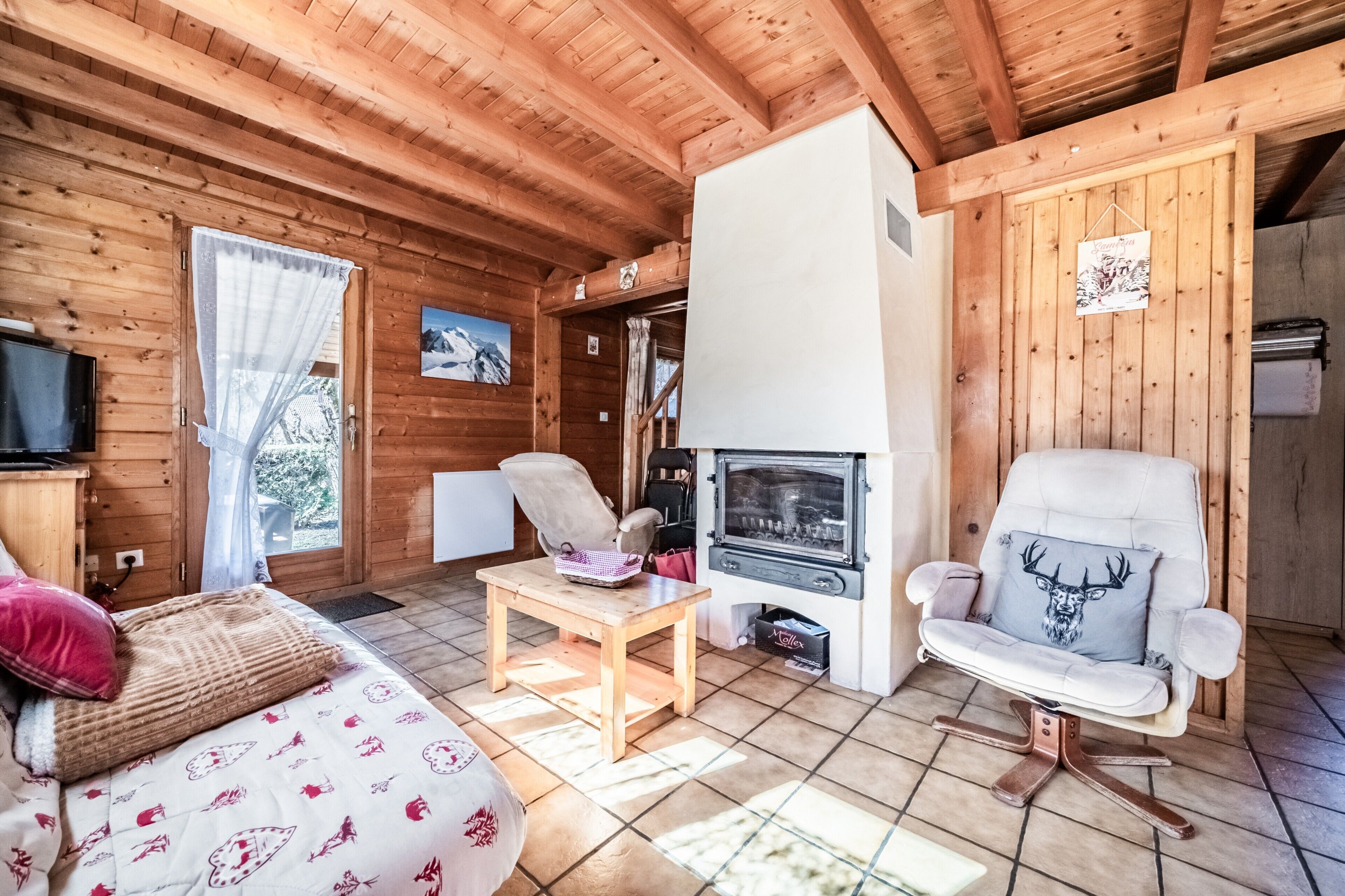 Interno di una baita in legno con divano, poltrona, tavolo, camino e televisore.