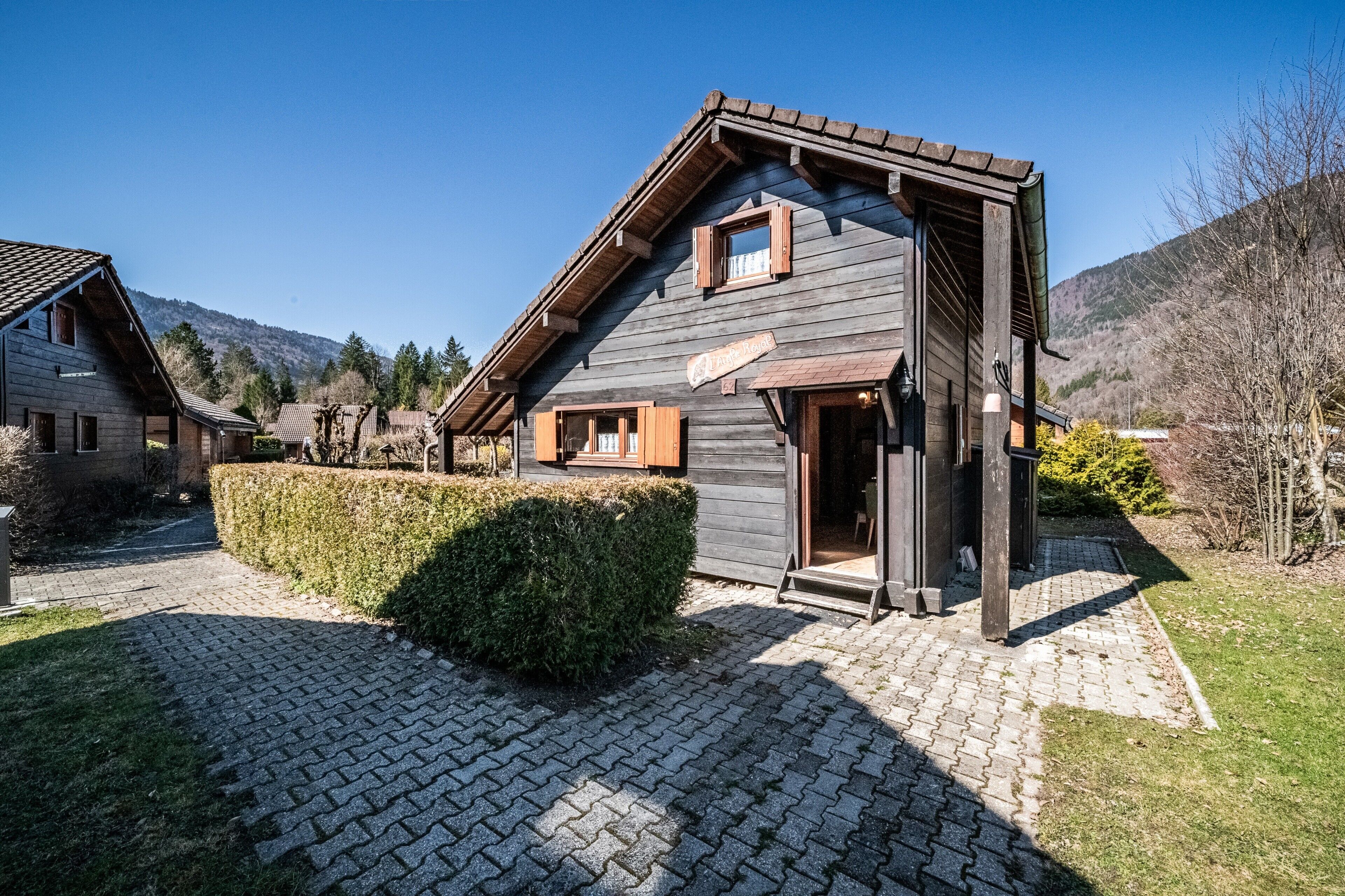Una casa a due piani in legno con tetto spiovente, un portico in legno e un vialetto lastricato.