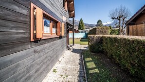 A wooden building with a paved pathway leading to a green area, a wooden fence, and a clear view of a mountain range. - Chalet "6p Comfort - The Royal Eagle" with Mountain View, Shared Terrace and Wi-Fi (Verchaix)