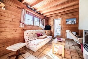 Ein Holzhäuschen im Inneren, mit einer Couch, einer Bank, einem Tisch, einem Fernseher und einem Kamin.