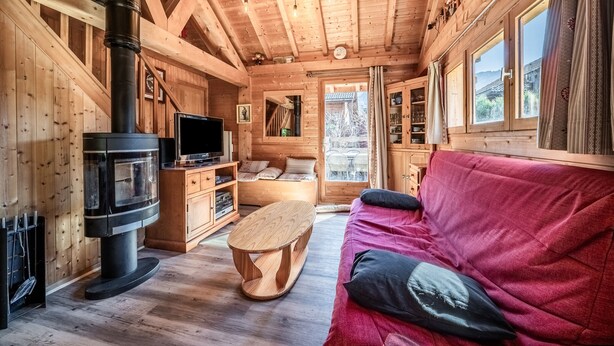 Ein Interieur einer Holzhütte mit Kamin, Fernseher, Holzmöbeln und einem roten Sofa.