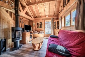 En stuga med träpanel på insidan, en öppen spis, en tv, trämöbler och en röd soffa.