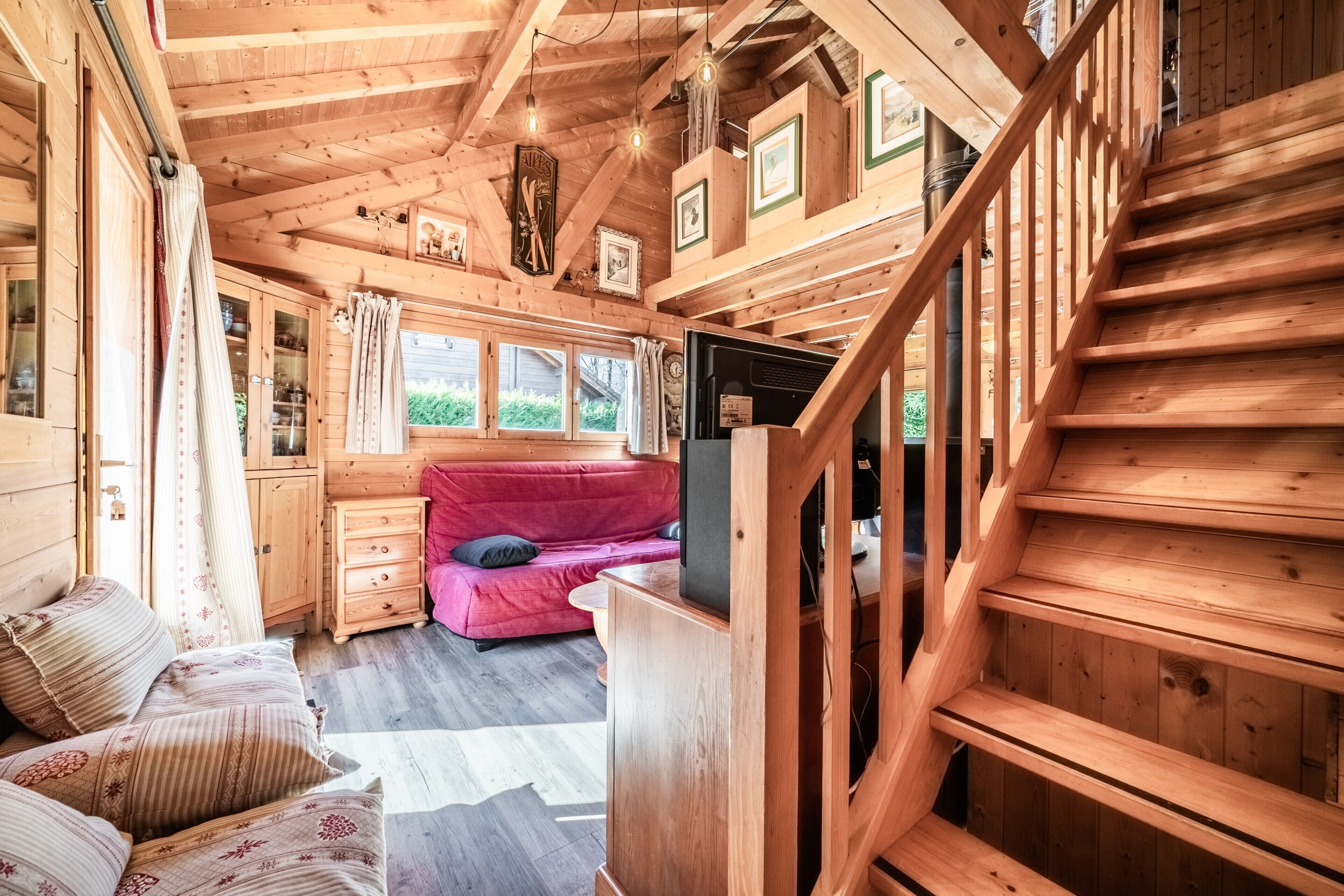A wooden cabin interior with a staircase, a red sofa, and a television.