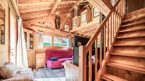 Ein Holzblockhaus-Innenraum mit einer Treppe, einem roten Sofa und einem Fernseher.