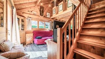 A wooden cabin interior with a staircase, a red sofa, and a television.