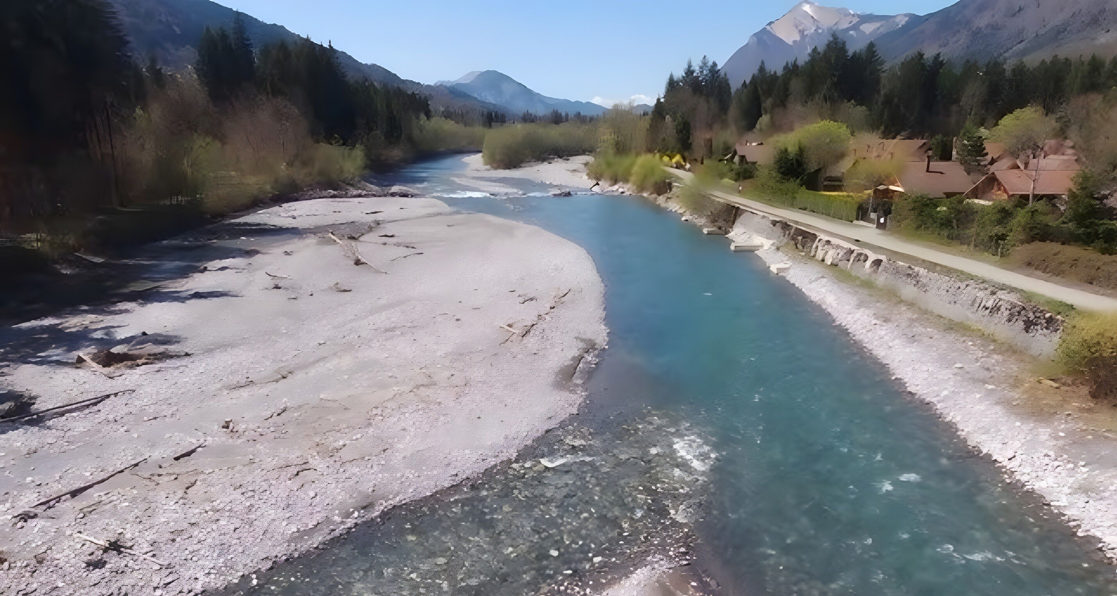 Un fiume con acque cristalline, una spiaggia sabbiosa e un ponte con edifici a destra.