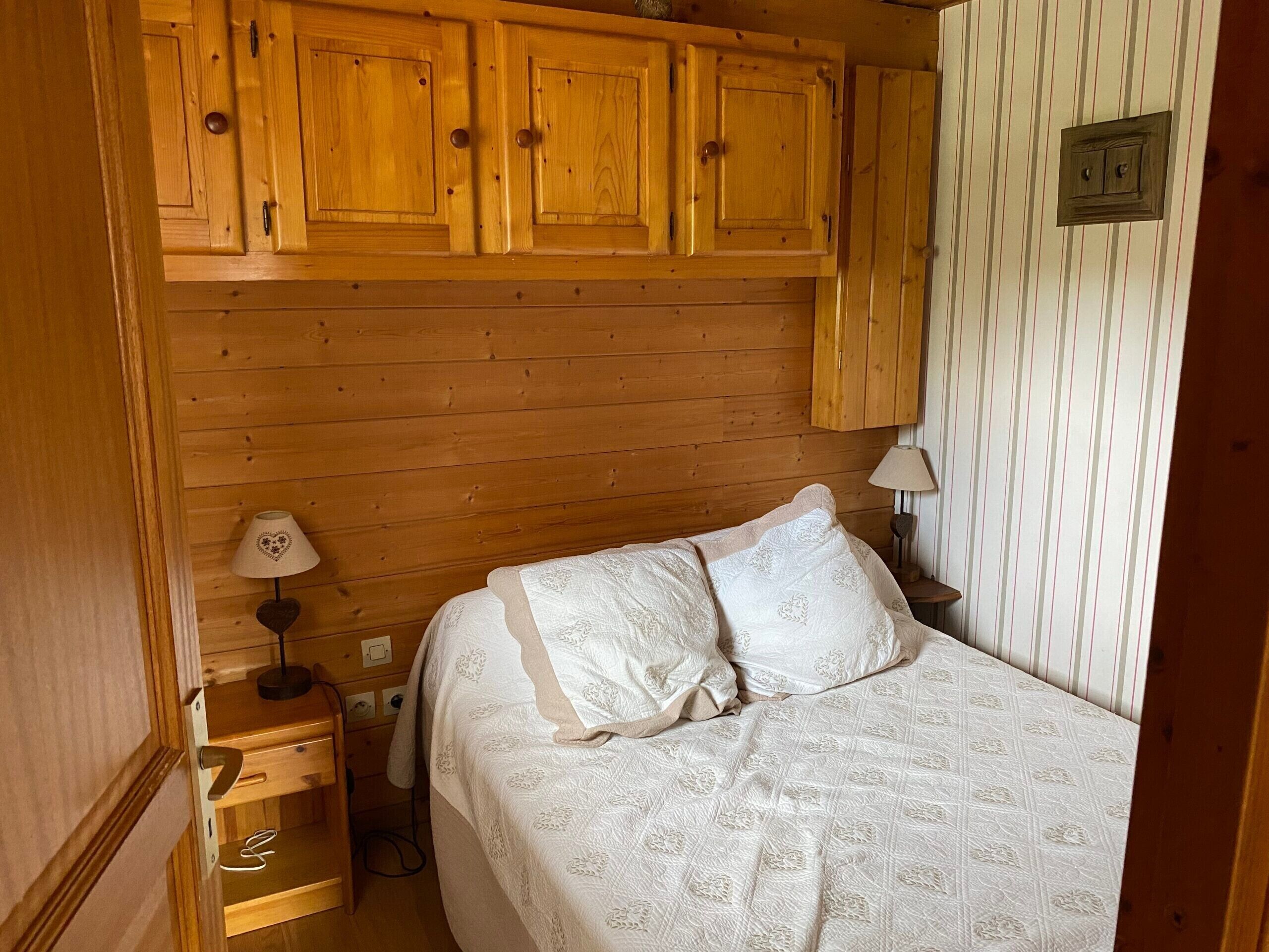 Una stanza con rivestimenti in legno, un letto, un comodino e una lampada.