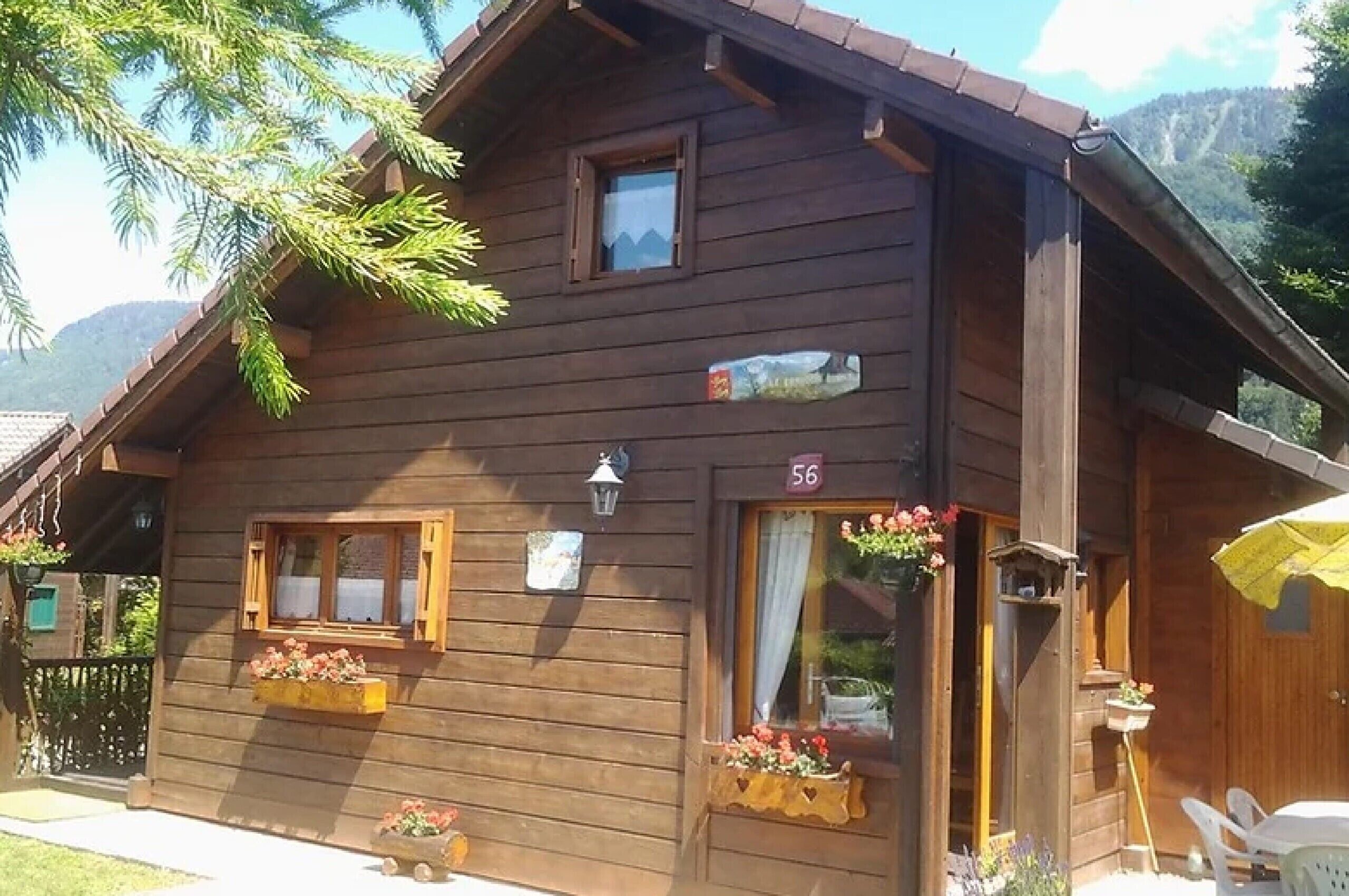 Una cabaña de madera con un cartel con el número '56', ventanas con jardineras y una puerta con cortina.