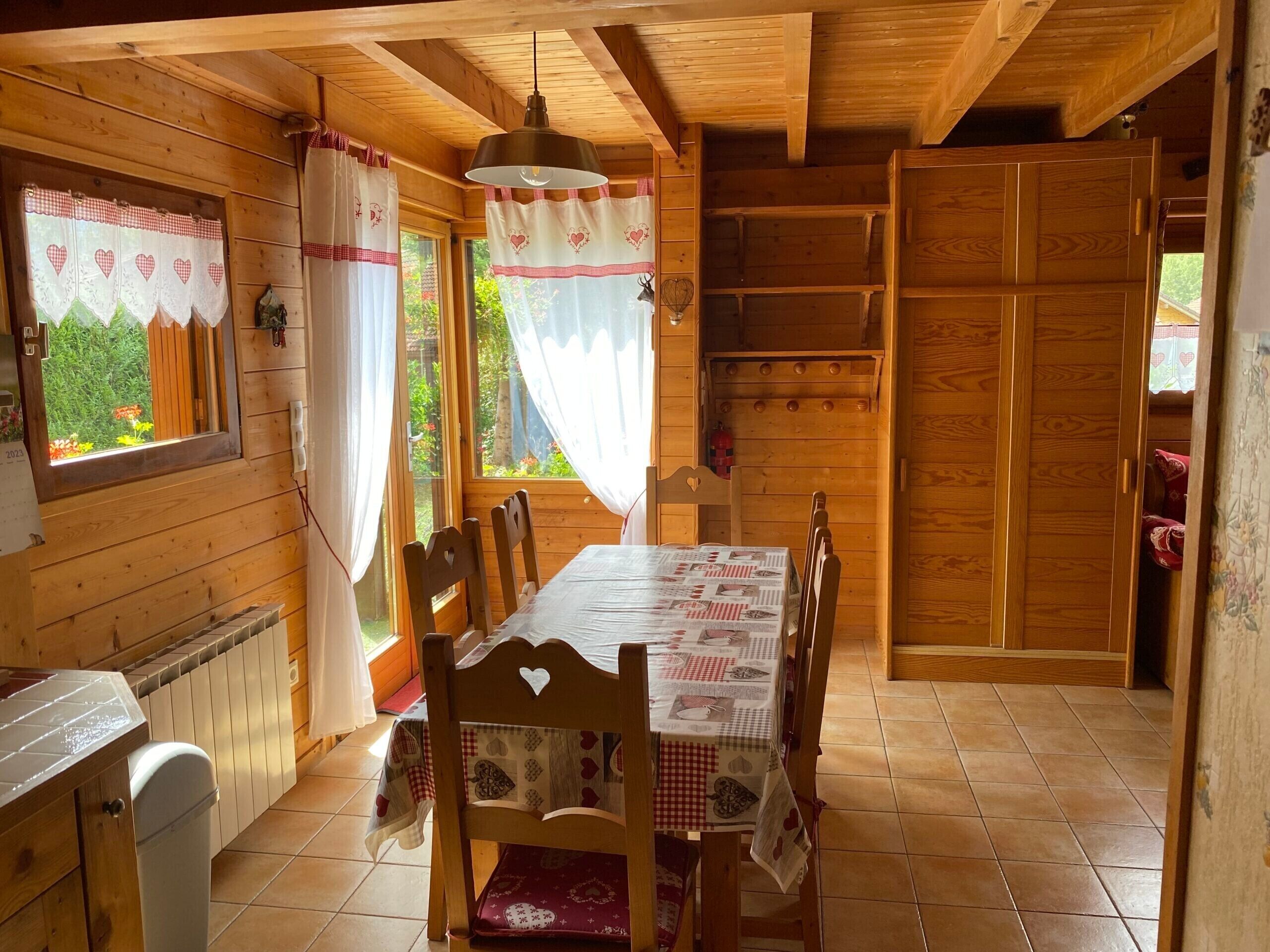 Una baita di legno con un tavolo da pranzo, sedie, un lampadario e una finestra con tende.