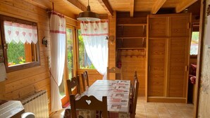 Una baita di legno con un tavolo da pranzo, sedie, un lampadario e una finestra con tende.