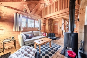 A wooden cabin interior with a sofa, a table, a fireplace, and a window with curtains. - Chalet "6p - Le Casse Noisette" with Shared Terrace and Wi-Fi (Verchaix)