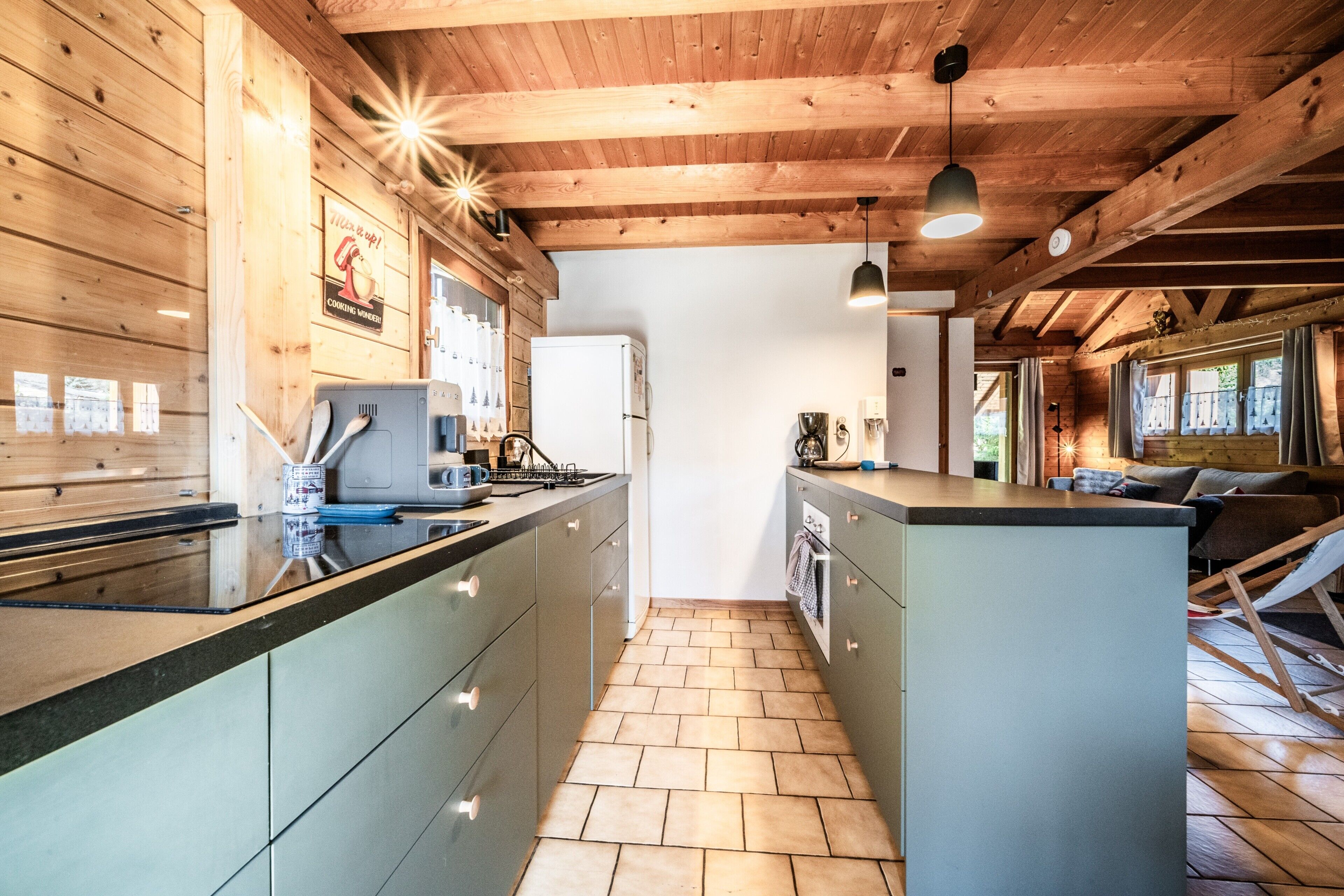 A modern kitchen with wooden beams, a central island, and a view to the living area.