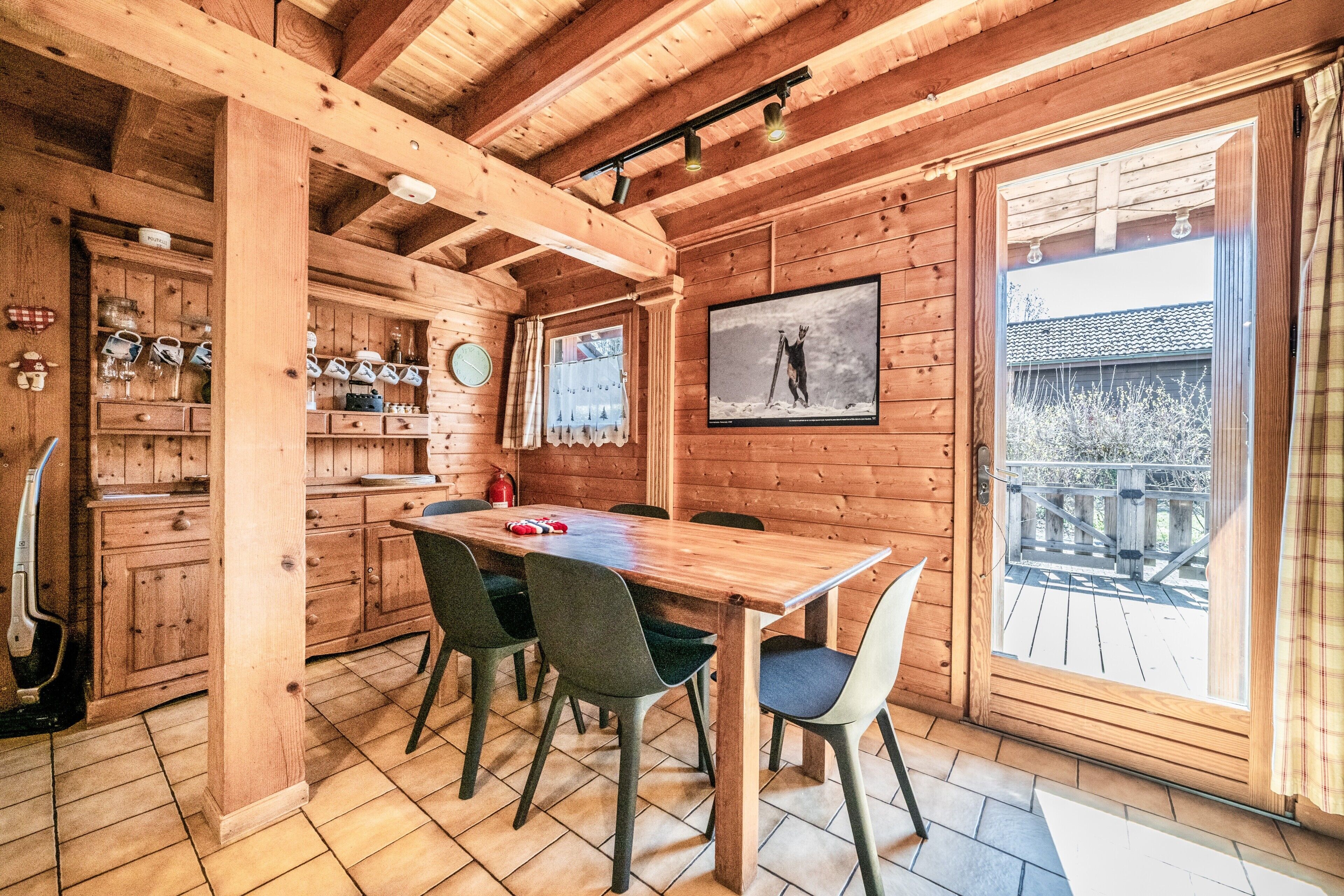 Un interior de madera con una mesa de comedor, sillas, una zona de cocina con estanterías y un amplio ventanal con vistas.