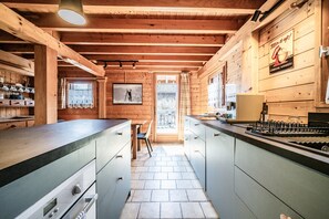 Una cocina tipo cabaña de madera con una isla central, una zona de comedor y vistas a través de una puerta.