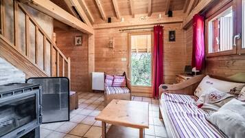 Interno di una baita in legno con un letto, un tavolo, una sedia e un camino.