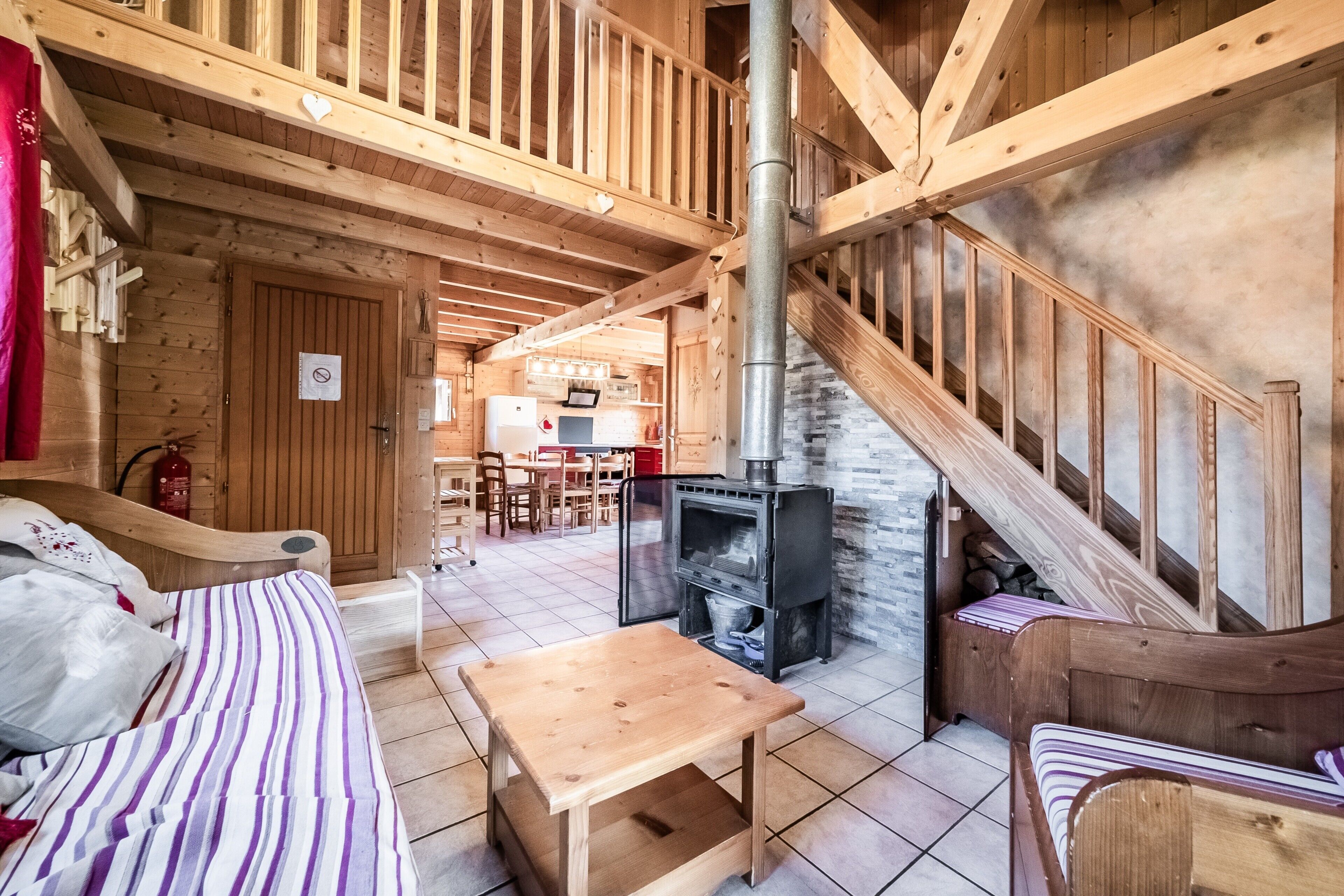 Un interior de madera con una cama, una pequeña mesa, un sofá, una escalera y una zona de cocina.