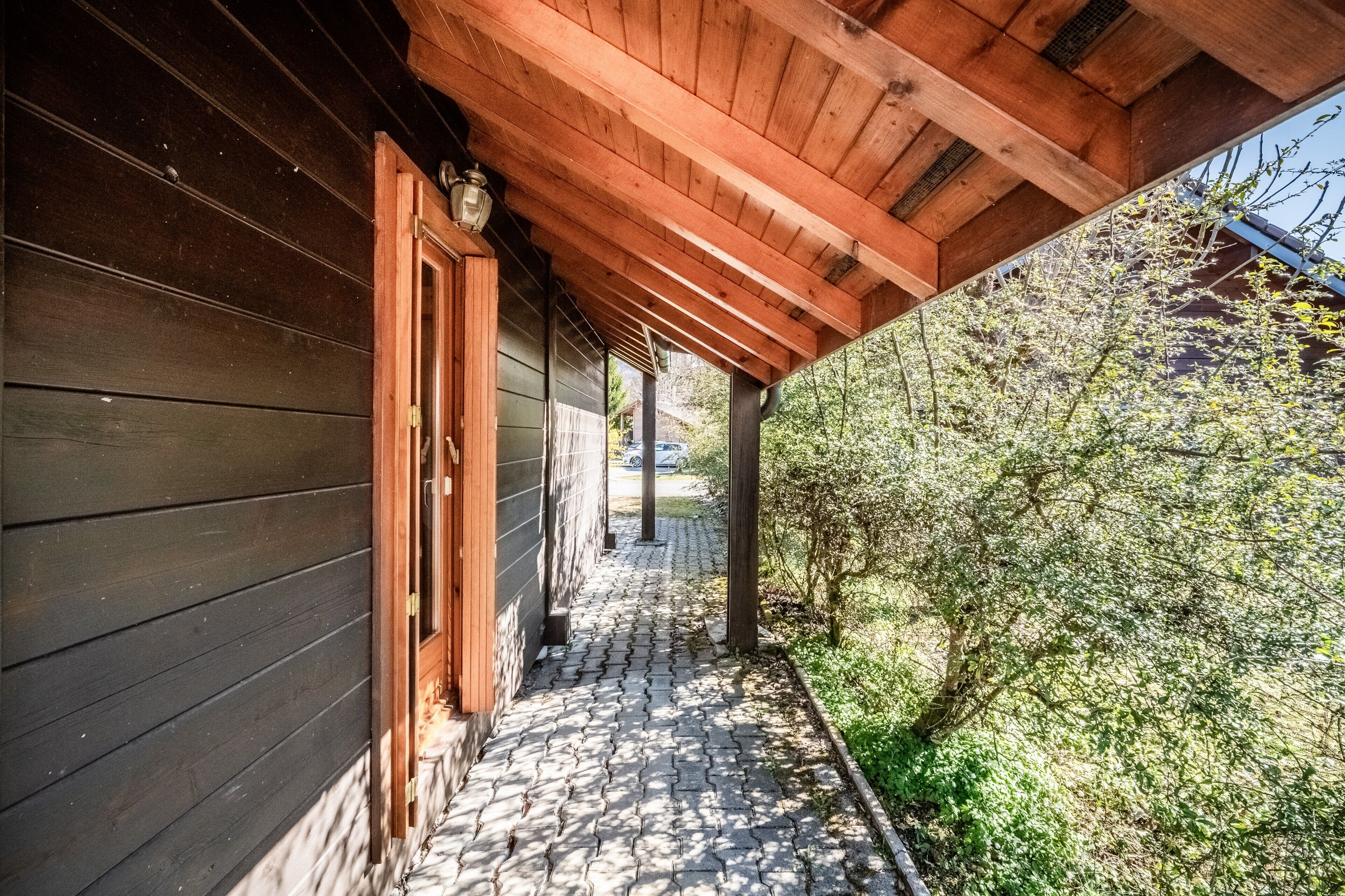 Facciata in legno con veranda coperta e vialetto lastricato che conduce a una porta.